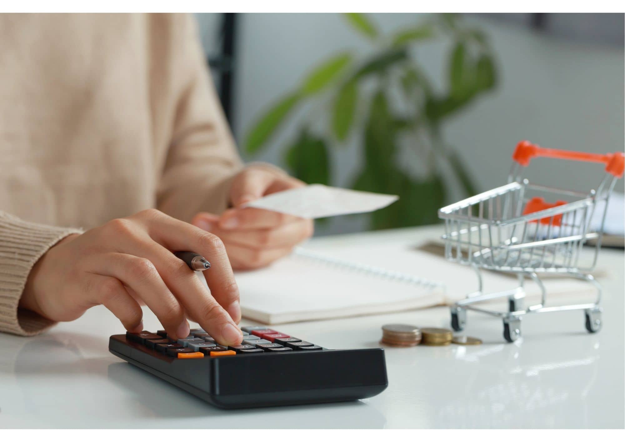 hand van vrouw typt op rekenmachine met klein winkelwagentje op de voorgrond