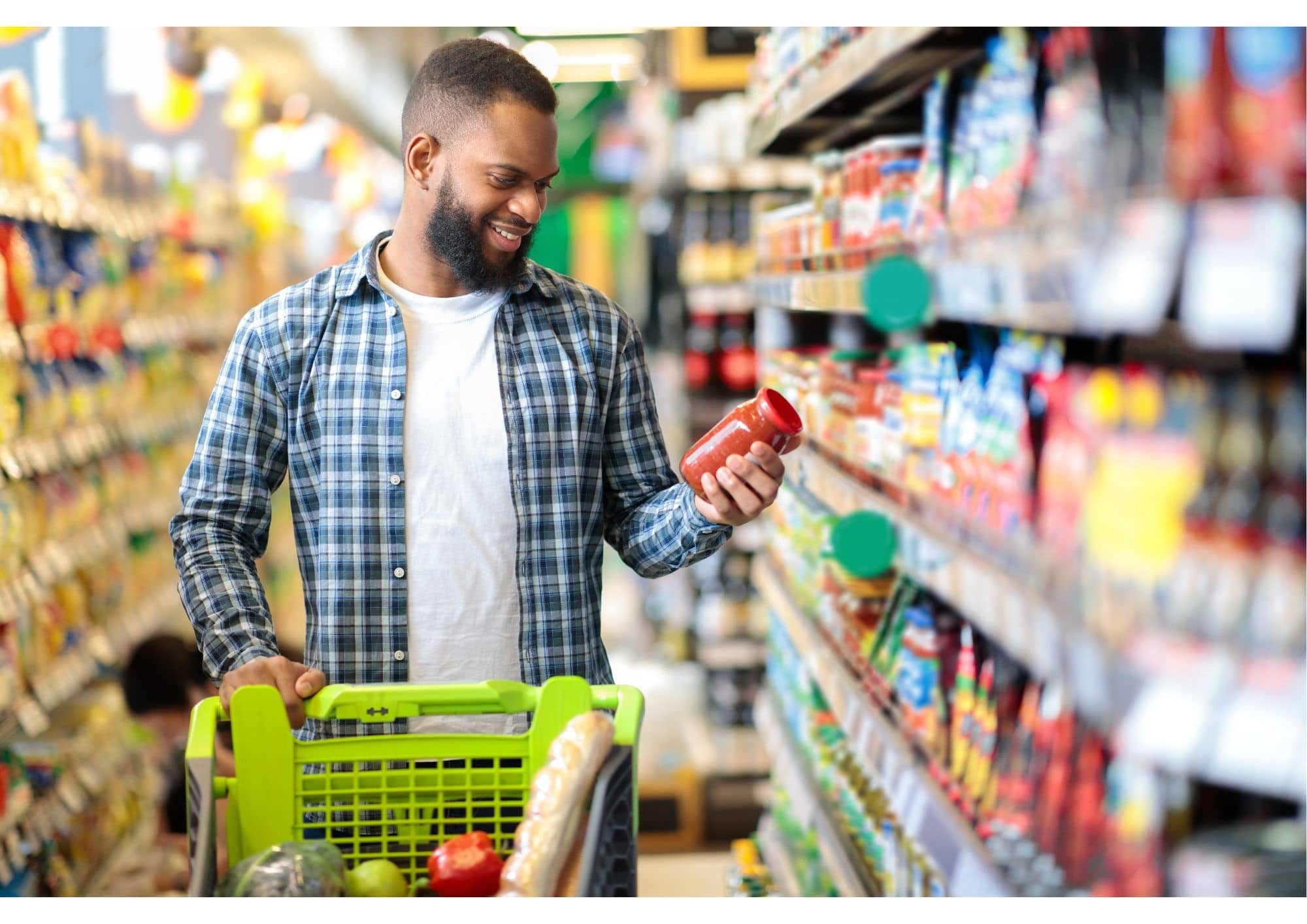Man in supermarkt met winkelwagentje en houdt een pot pastasaus in zijn hand