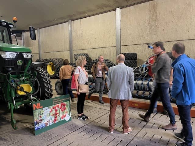 Vijf mensen die in een hal naast een tractor staan en kijken naar een machine