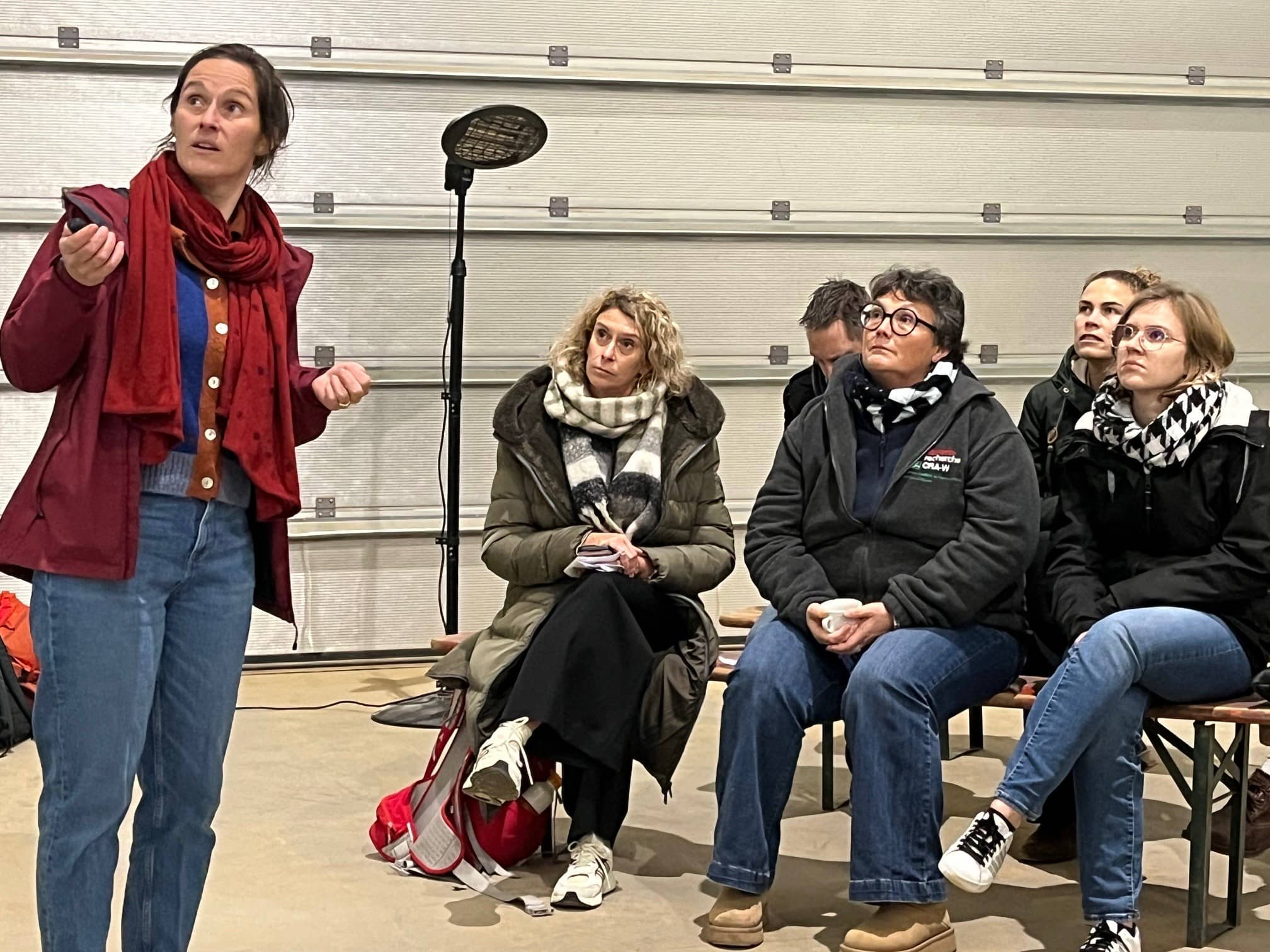 een vrouw kijkt naar het scherm terwijl zij aan een groep mensen, die op een bank zitten, een presentatie geeft
