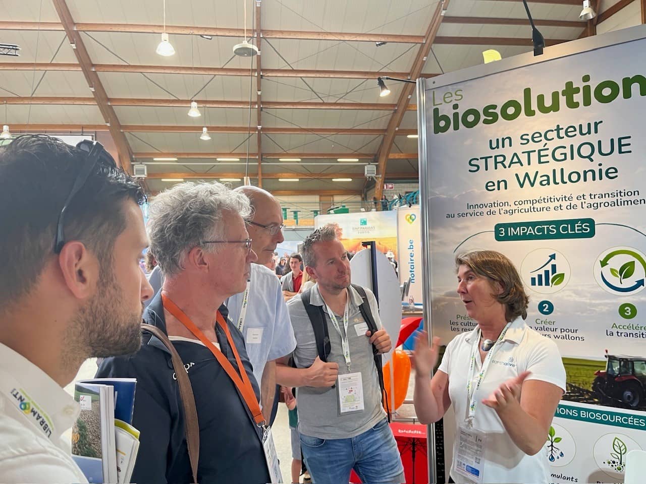 een aantal mannen luistert naar een vrouw die op een beurs voor een banner van Biosolutions uitleg geeft