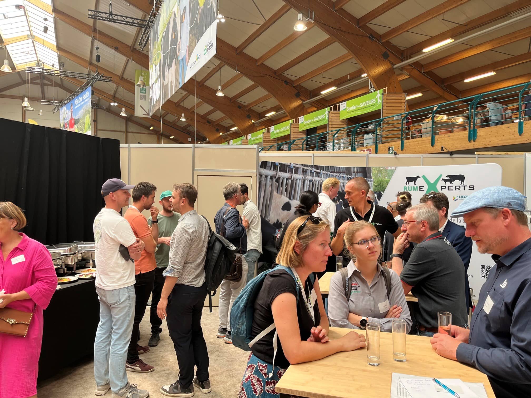 een 15-tal mensen staan op een beurs rond hoge sta-tafels te eten en te praten