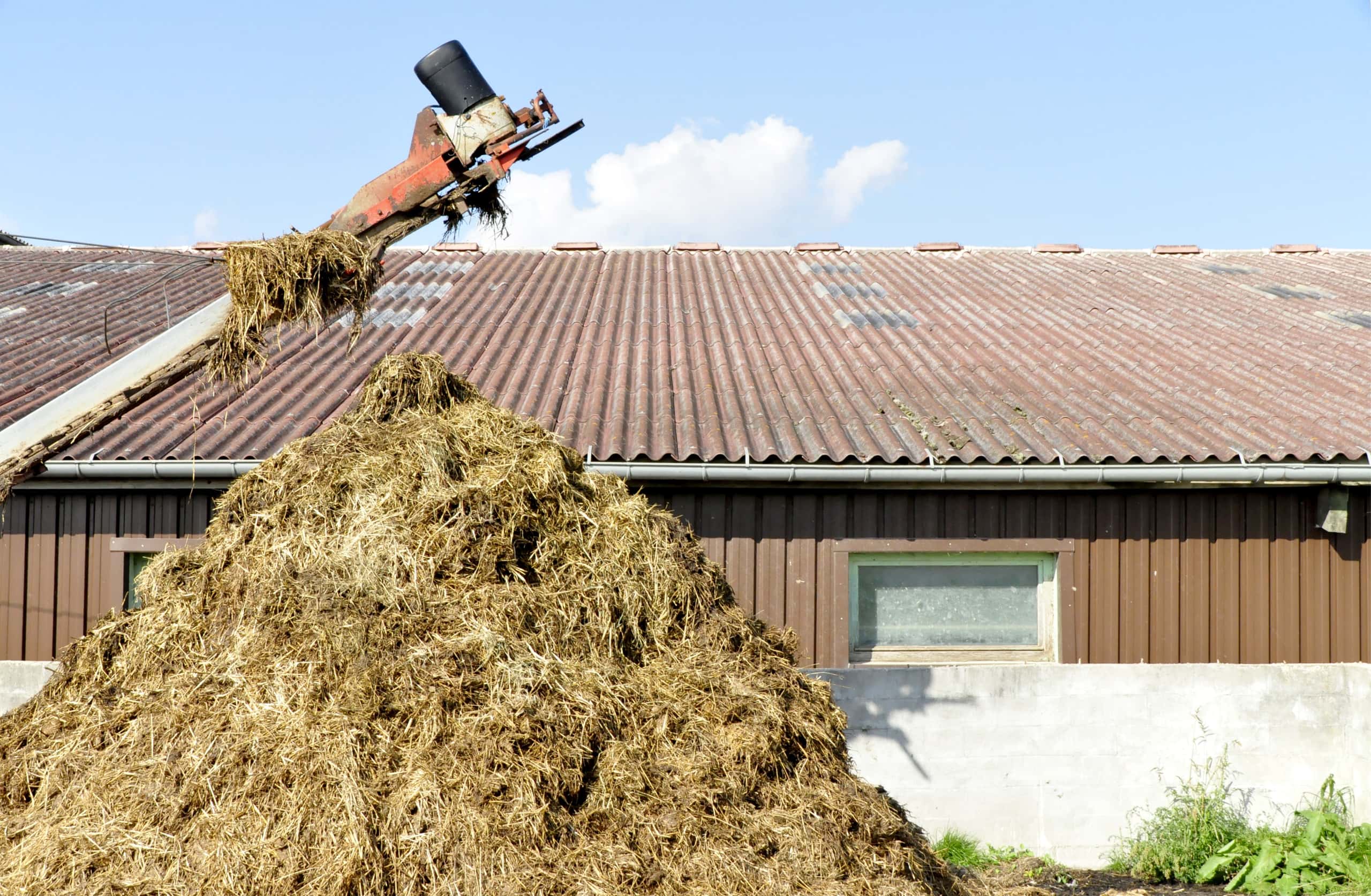 a machine scooping a pile of manure in front of a barnhouse