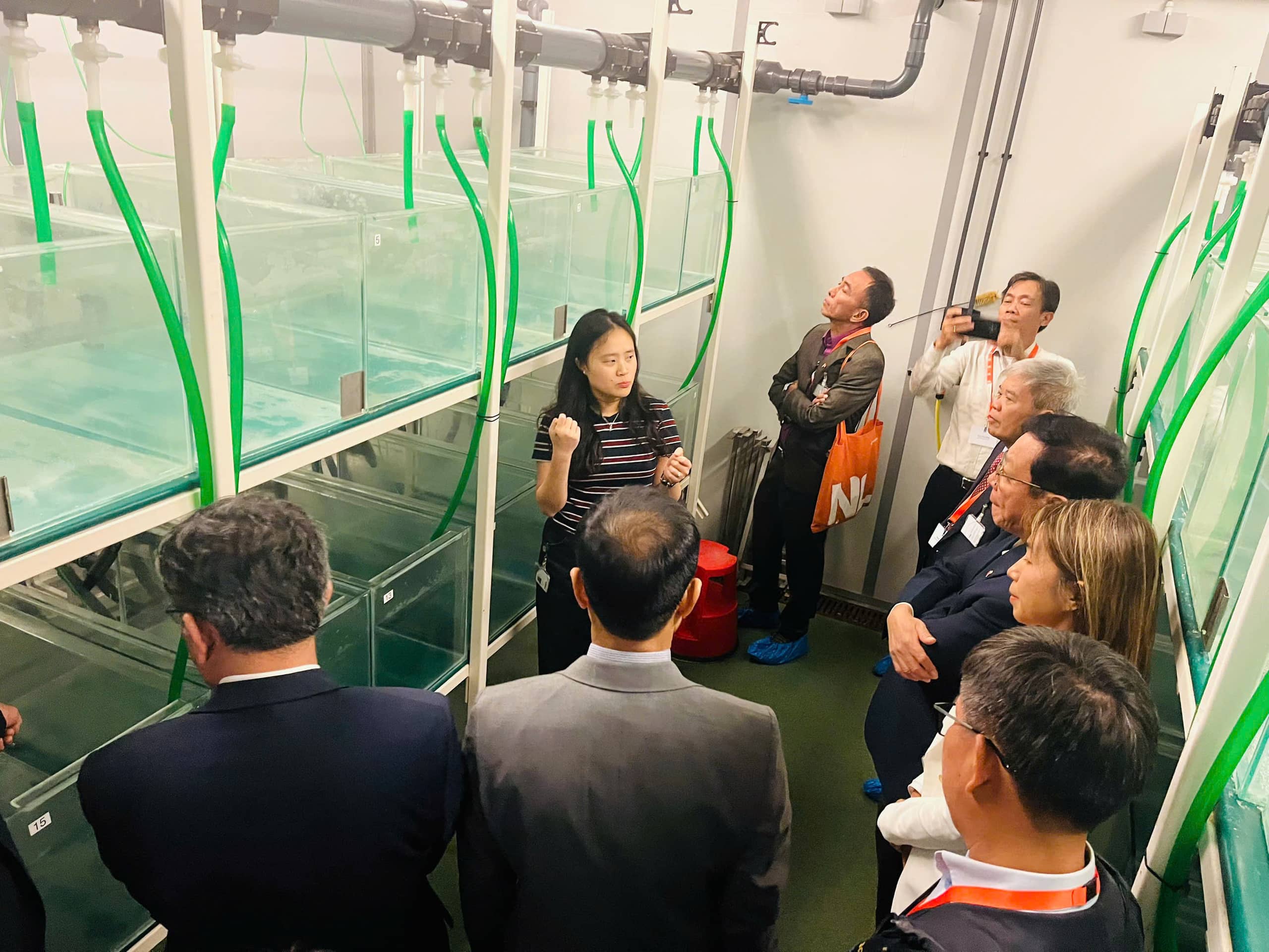 group of 7 people in demonstrating lab, big tanks of water, 1 person explaining to the other