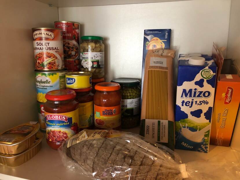 A cupboard stocked with non-perishable food like pasta, rice, canned vegetables, long-life milk and other food products.