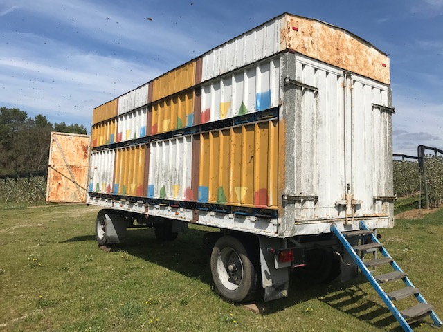 A trailer carrying beehives parked next to an orchard