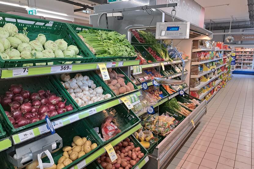 Grocery store in Hungary. A fruits and vegetables aisle is shown with other groceries in the background. There is a fridge with fresh vegetables, there is also a hanging scale.