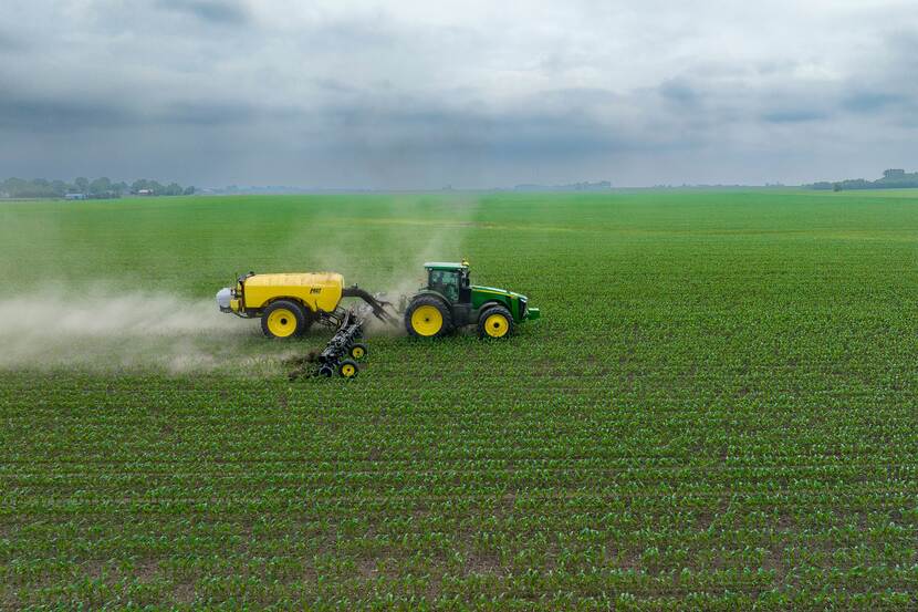 A tractor in a green field pulls a trailer which is spraying nitrogen fertilizer