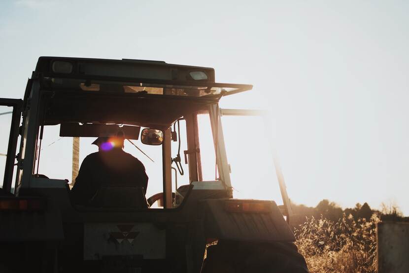 Tractor driver driving a tractor in the field. Also, the sun is setting in the background.