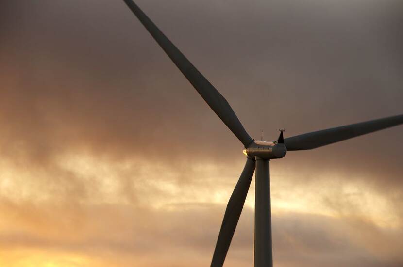 A wind turbine can be seen against the backdrop of a cloudy sky lit by the setting sun