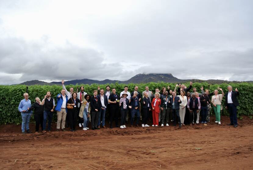 A group of people pose for a photo standing in front of a tomato orchard with a mountain in the background and overcast weather