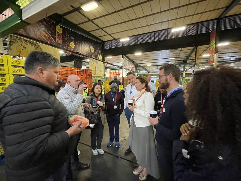Group of people stand and talk in a circle while visiting a produce market in Johannesburg, South Africa