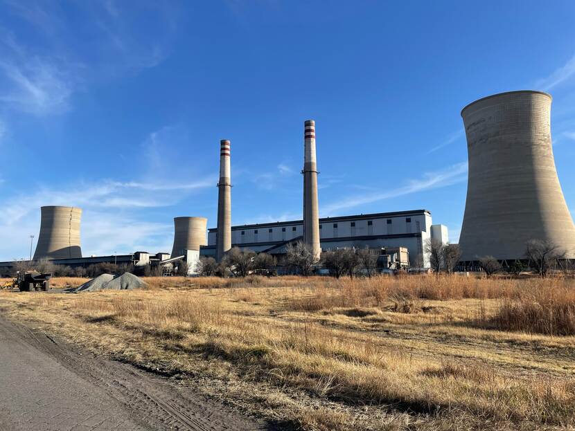 A coal power station with two cooling towers on the left, two chimneys in the middle, and a cooling tower on the right. In the foreground is a field of grass.