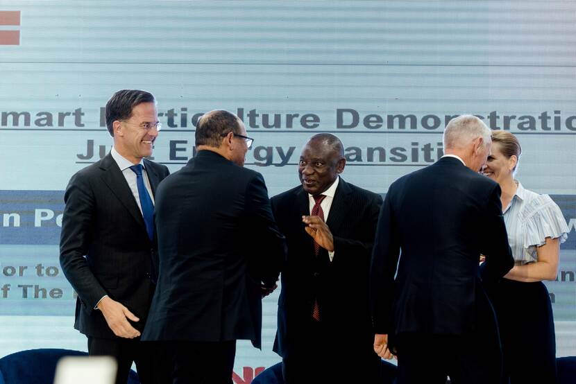 Facing the camera, Prime minister of Netherlands on stage with South African president and Danish prime minister as they shake hands with Eskom CEO and Dutch Ambassador who have their backs to the camera.