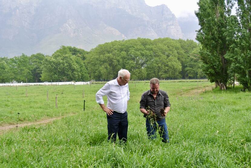 Two men stand in a field to inspect soil conditions.